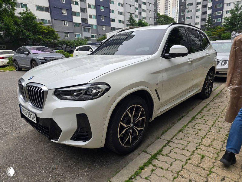 Белый BMW X3 20i XDrive на парковочном месте, вид под углом; заметны боковые линии кузова, диски и чёрные элементы отделки.