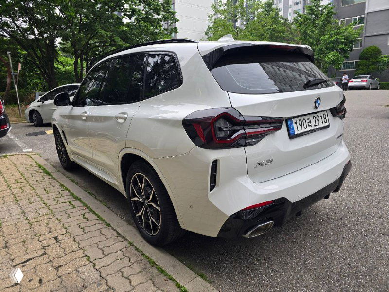 Задняя часть BMW X3 с лёгким разворотом — видна форма фонарей, бампер и выхлопная система на фоне жилого двора.