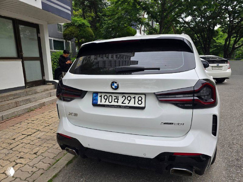 Ещё один ракурс задней части белого BMW X3 20i XDrive MSport, видно шильдик модели, задние фонари и корейский номерной знак на бампере.