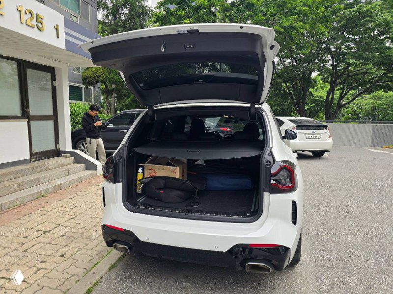 Открытый багажник BMW X3 показывает пространство и комплектное оборудование; внутри размещены предметы и запасное колесо видно частично.