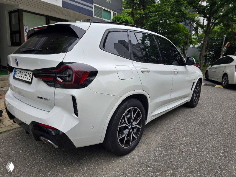 Тёмные боковые элементы и задний угол кузова белого BMW X3 20i на парковке; видны контуры крыльев и колёс с дизайном дисков.