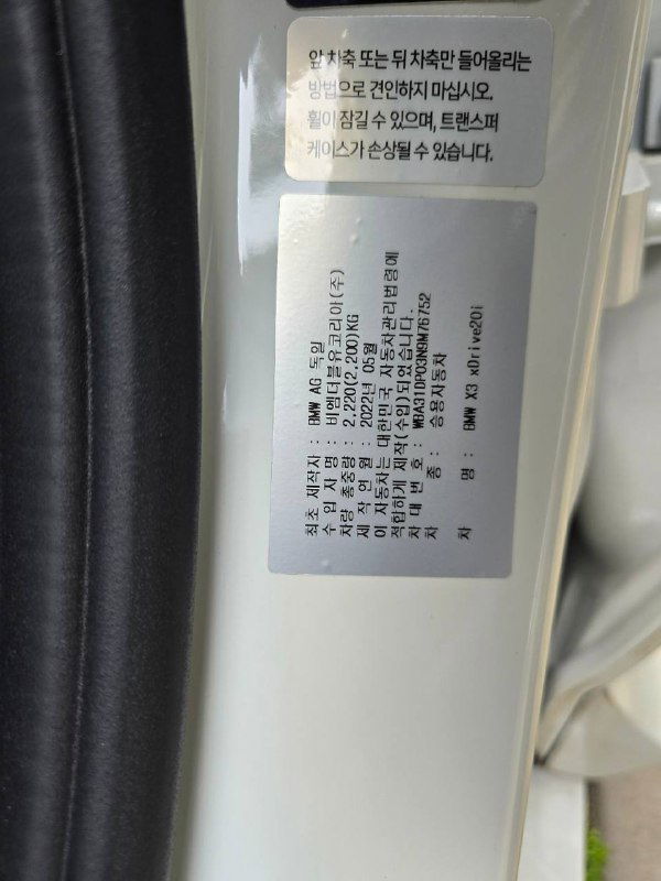 Наклейка с технической информацией на стойке двери BMW X3: табличка с данными на корейском языке и частью VIN/серийной информации.