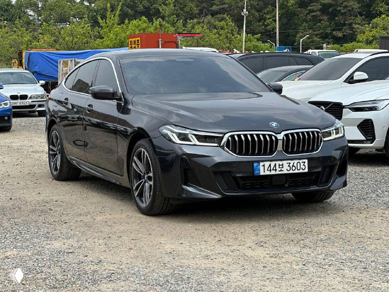 Боковой ракурс BMW GT 620D, видна линия купе-образного силуэта, затемнённые стекла и экономичная парковка среди других автомобилей.