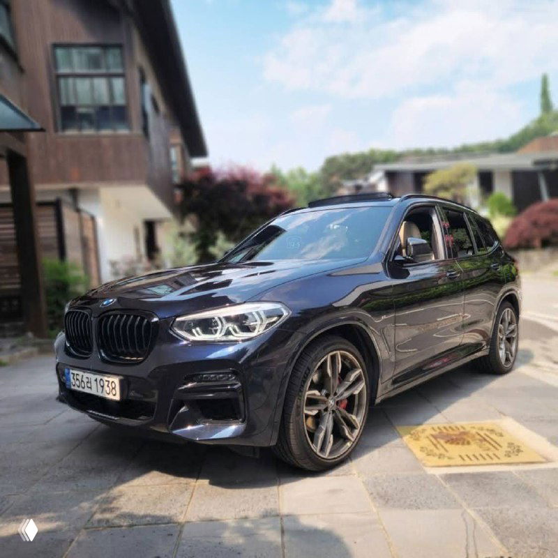 BMW X3 M40i на угловом ракурсе спереди: видны передний бампер, фары, колёса и отражения окружения на глянцевом лаке кузова.