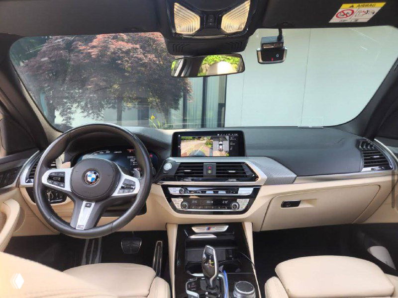 Интерьер BMW X3 M40i: вид на переднюю панель, медиасистему, руль и элементы отделки — светлая кожаная обшивка и хромированные вставки.