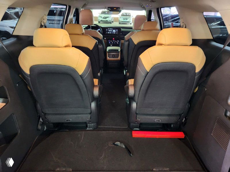 Панорамный вид внутри KIA Carnival: второй и третий ряд сидений, бежево‑чёрная обивка и свободное пространство багажника, салон дилерского состояния.