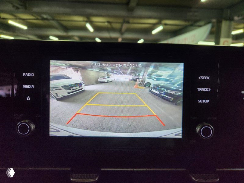 Экран задней камеры KIA Carnival с линиями разметки при парковке, на экране видно паркинг и окружающие автомобили в закрытом помещении.
