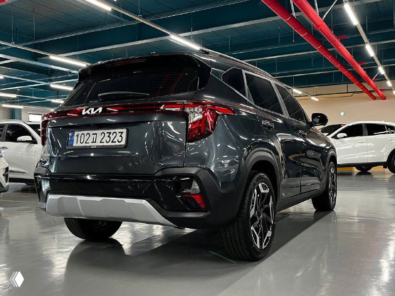 Вид сзади и в профиль на серый Kia Seltos Signature 2024 в автосалоне; видны задние фонари, форма бампера и общий силуэт кроссовера.