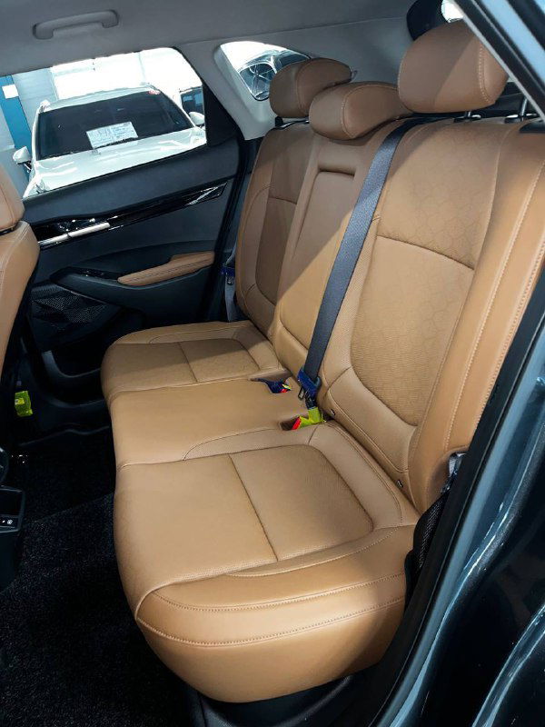 Фотография задних сидений Kia Seltos Signature 2024 с коричневой кожаной обивкой, видны ремни безопасности, центральный складной подлокотник и отделка дверей.