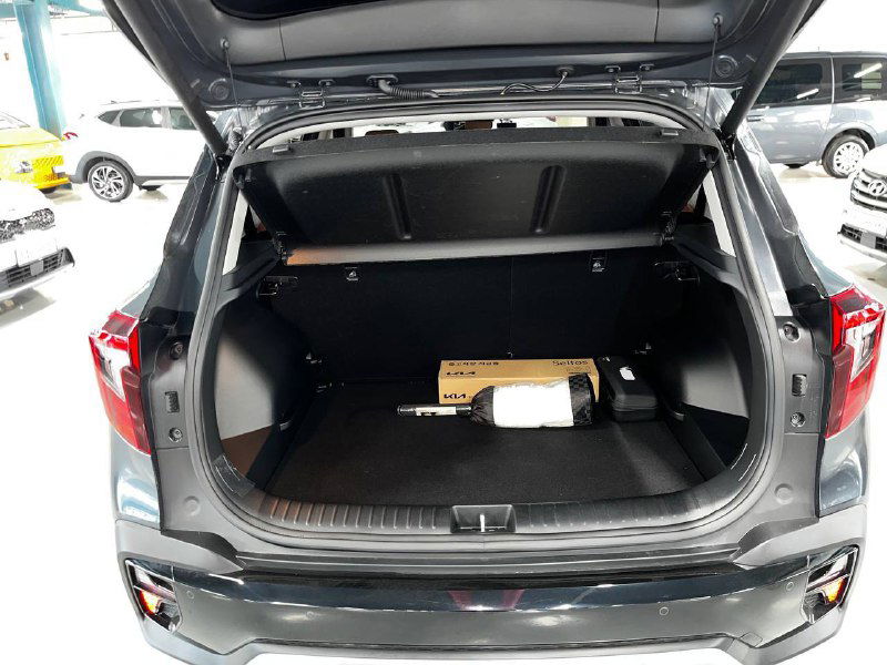 Открытый багажник Kia Seltos Signature 2024 с показанным объёмом и полкой; внутри видна упакованная коробка и ровное пространство для поклажи.