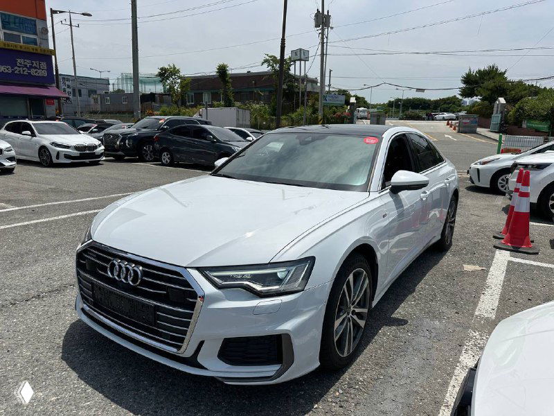 Ауди A6 45 TFSI, три четверти спереди слева, белый кузов, колёса и детали бампера хорошо видны на парковке.