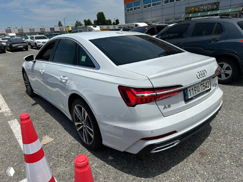 Угловой вид сзади слева белой Audi A6, видна форма багажника, фонари и состояние левого борта автомобиля.
