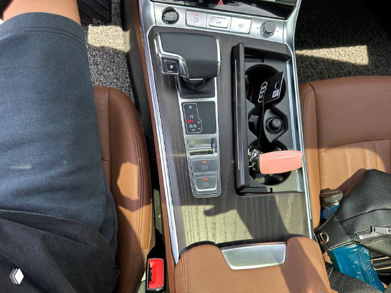 Крупный план центральной консоли Audi A6: селектор коробки, подстаканники и декоративные вставки в салоне, вид детали интерьера.