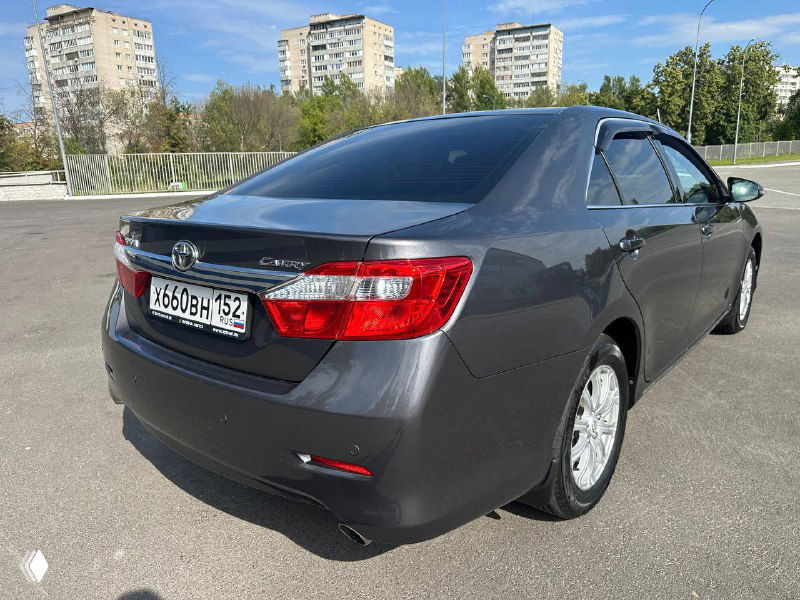 Вид сзади и правого бока серой Toyota Camry V50; чистый кузов, отражение зданий на лаке и задние фары без видимых дефектов.