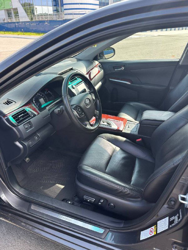 Фото водительского места с открытой дверью: видны регулировки сиденья, напольный коврик и аккуратная обшивка салона в светлых условиях.