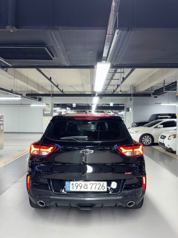 Вид сзади чёрного Chevrolet Trailblazer в освещённом подземном паркинге: видны задние фары, багажник и выхлопные патрубки на машине.