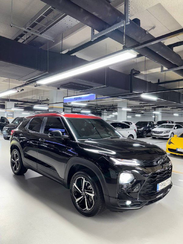 Чёрный Chevrolet Trailblazer под углом в паркинге: заметны дизайн передней части, красная декоративная вставка на крыше и стильные диски.