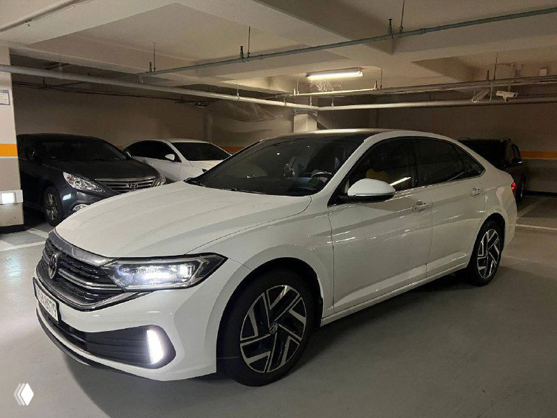 Фронтально‑боковой ракурс белой Volkswagen Jetta в паркинге; видны диски, дневные ходовые огни и боковой профиль кузова.