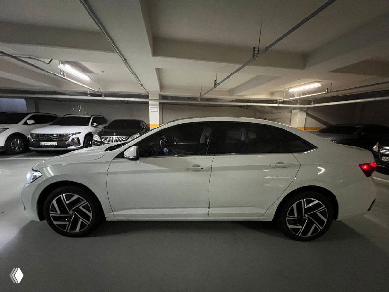 Боковой профиль белой Volkswagen Jetta в подземной стоянке; видны линии кузова, колёсные диски и габариты автомобиля.