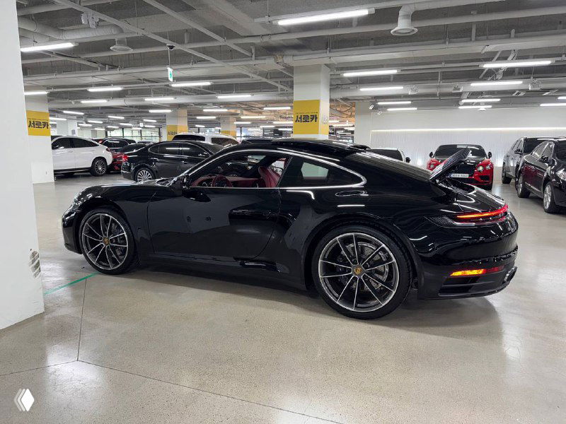 Черный Porsche 911 Carrera 2021, боковой ракурс в парковочном помещении; видно профиль кузова, легкосплавные диски и оформление задней части.