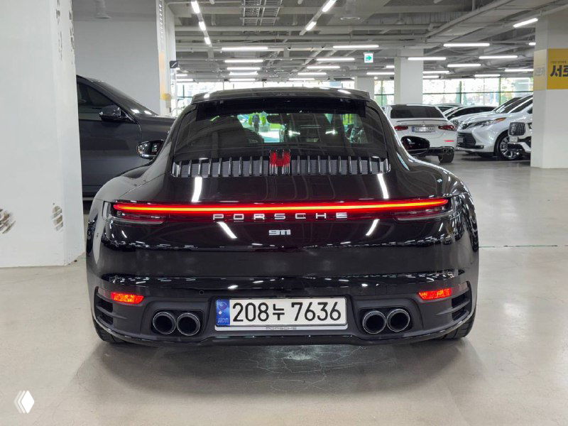 Задняя часть Porsche 911 Carrera: светящаяся LED-лампа «Porsche», двойной выхлоп и корейский номер на стоянке автосалона.