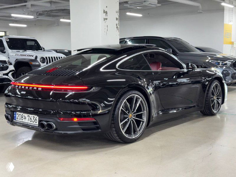 Porsche 911 Carrera, вид сзади на стоянке; заметны линии кузова и фон других автомобилей в автосалоне, высокое качество лакокрасочного покрытия.