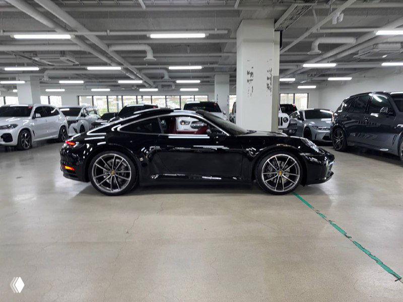 Черный Porsche 911 Carrera, полный боковой профиль справа; снимок в помещении демонстрирует клиренс и посадку автомобиля.