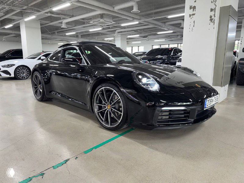 Фронтальный угол Porsche 911 Carrera в автосалоне; видно переднюю оптику, капот и часть колесной арки на фоне других авто.