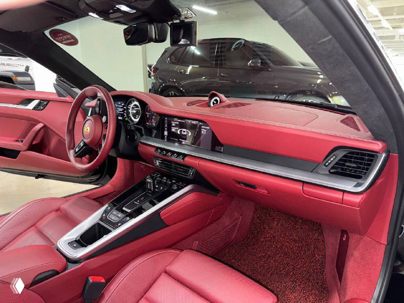 Интерьер Porsche 911 Carrera с красной кожаной отделкой сидений, панелью приборов и центральной консолью в крупном плане в салоне.
