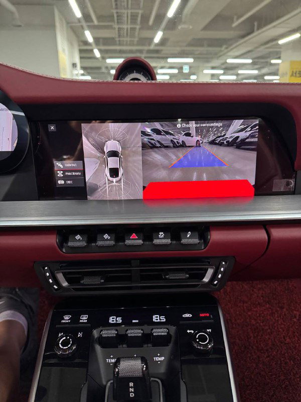 Крупный план дисплея и системы камеры заднего вида в Porsche 911; на экране вид парковки, элементы управления на торпеде.