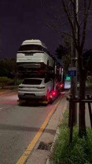 Многоуровневый автовоз с несколькими автомобилями (Kia, Genesis и другие) на ночной дороге, видны верхние и нижние ряды машин и дорожная обстановка.