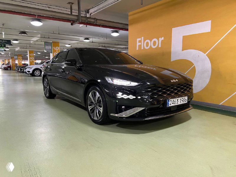 Профиль чёрного Kia K8 в подземной паркинговой зоне рядом с отметкой Floor 5, видна литая резина и боковой силуэт автомобиля