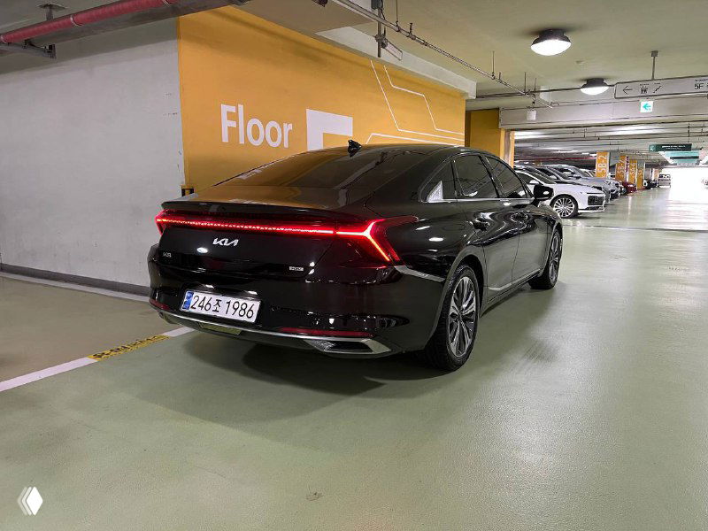 Задний трёхчетвертной вид Kia K8 — красная световая полоса на задней части и общий силуэт седана в освещении паркинга