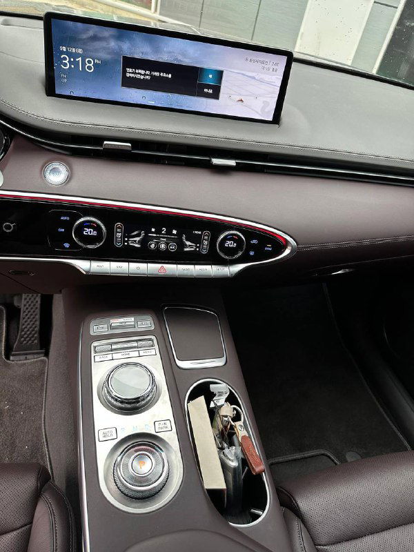 Крупный план центральной консоли Genesis GV70: селектор режимов, ручки управления климатом и экран приборной панели в зоне водителя.