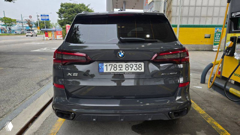 Задняя часть BMW X5 40D 2022 на стоянке у колонки, видна модель X5, интегрированные фонари и номерной знак на фоне АЗС.