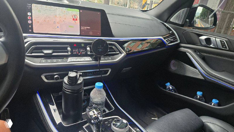 Салон BMW X5 40D 2022: центральная консоль, мультимедиа-дисплей и элементы управления, видны бутылки и личные вещи в подстаканниках.