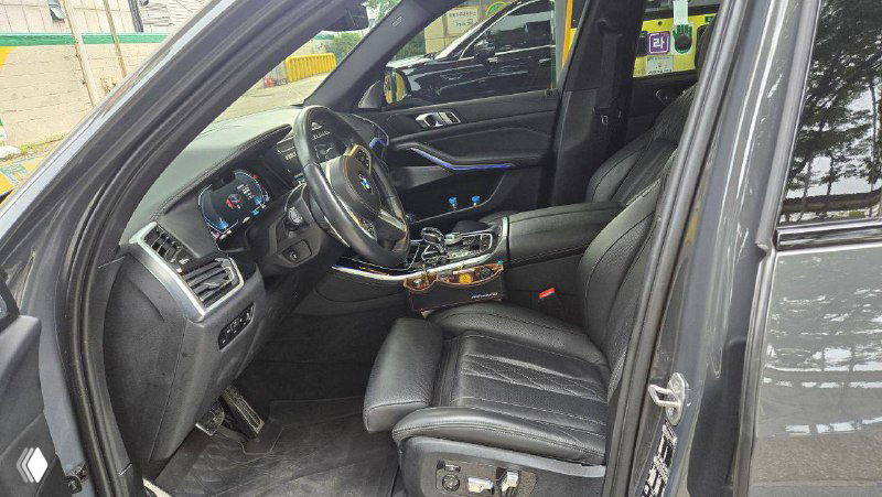 Водительское место BMW X5 40D: чёрные кожаные сиденья, многоступенчатая регулировка и вид на руль и приборную панель крупным планом.