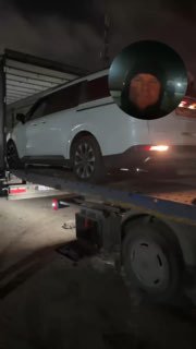 Белый минивэн Kia Carnival загружается на трейлер ночью, виден боковой профиль автомобиля и часть прицепа с открытой тентованной крышей.