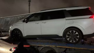 Крупный кадр боковой части белого минивэна на площадке, видны колёса и нижняя часть кузова, кадр снят при искусственном освещении.