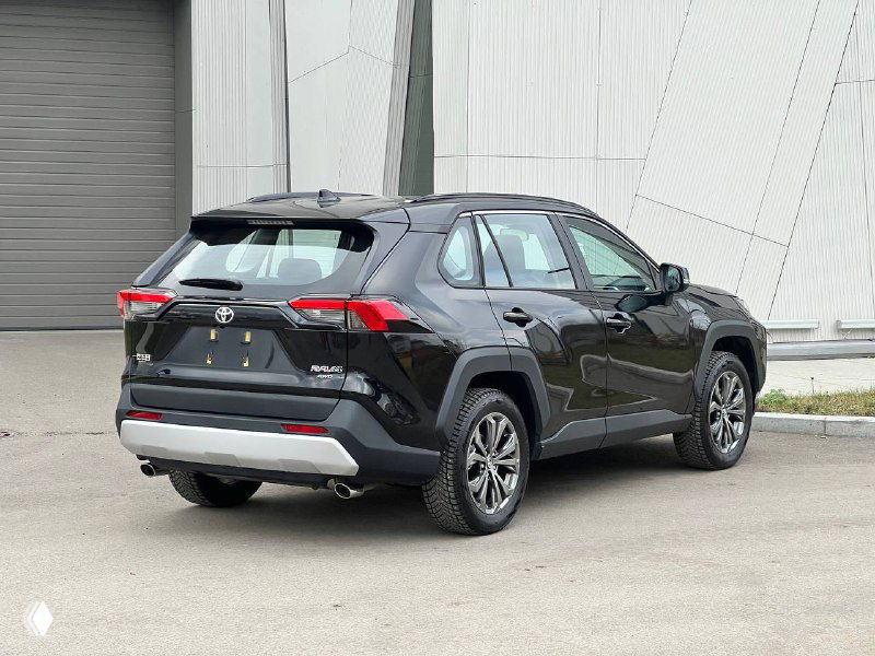 Toyota RAV4 2025, вид сзади под углом: задние фонари, бампер и общие пропорции кроссовера на фоне здания.