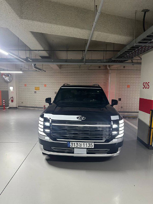 Hyundai Palisade 2025 крупным планом спереди в подземном паркинге; видна решётка радиатора и подключённые дневные ходовые огни.