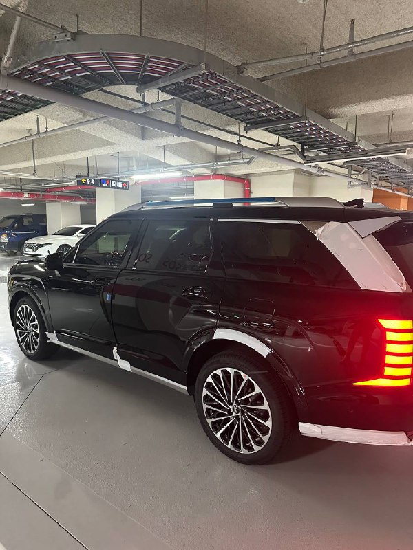 Чёрный Hyundai Palisade 2025, вид сбоку‑сзади в паркинге; заметна зеркальная отделка и тёмный кузов автомобиля.