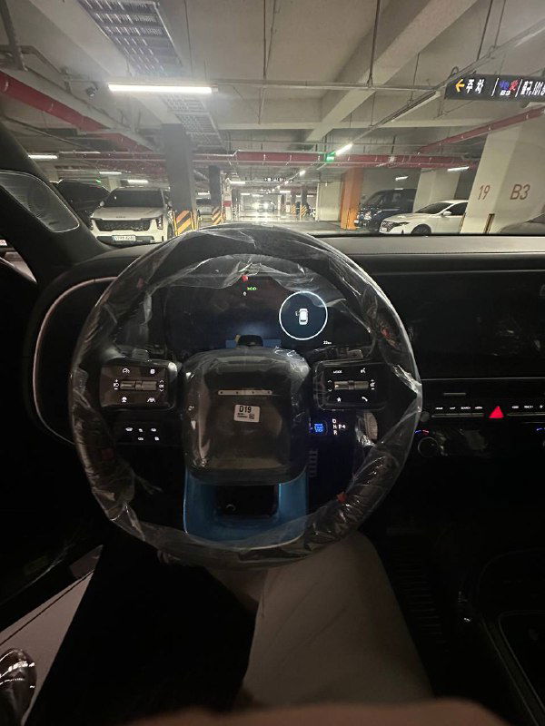 Вид на руль и приборную панель Hyundai Palisade 2025 с защитной плёнкой на рулевом колесе; салон новый, элементы управления видны.