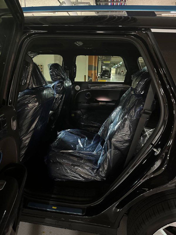 Задние пассажирские сиденья Hyundai Palisade 2025 в плёнке, вид в профиль через открытую дверь; интерьер выглядит новым и неиспользованным.