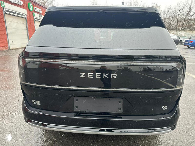 Задняя часть Zeekr 9X с эмблемой ZEEKR на крышке багажника и отсутствием регистрационного номера, вид на мокрой парковке