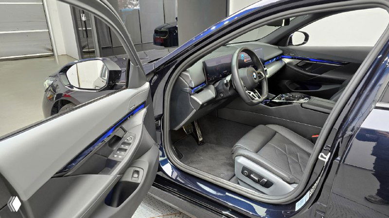 Открытая водительская дверь и вид на салон BMW 5‑Series 530i xDrive M Sport 2025, вид сбоку на переднее сиденье и отделку дверной панели, всё в хорошем состоянии