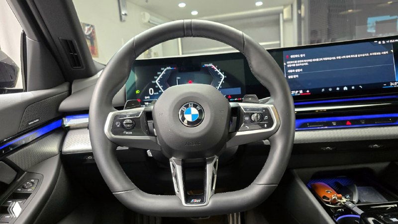 Руль и передняя панель BMW 5‑Series 530i xDrive M Sport 2025 — крупный план руля с кнопками, мультимедиа экран справа и отделка передней панели