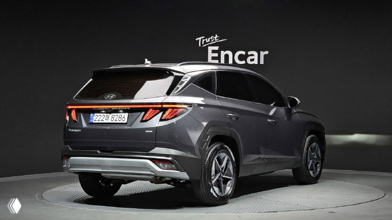 Вид сзади и правого бока Hyundai Tucson 2025, серый кузов, задние фонари и диффузор на фоне световой студии демонстрации.