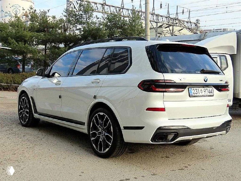 Вид сзади белого BMW X7: задние фонари, диффузор и выхлопные патрубки, автомобиль припаркован на сервисной территории
