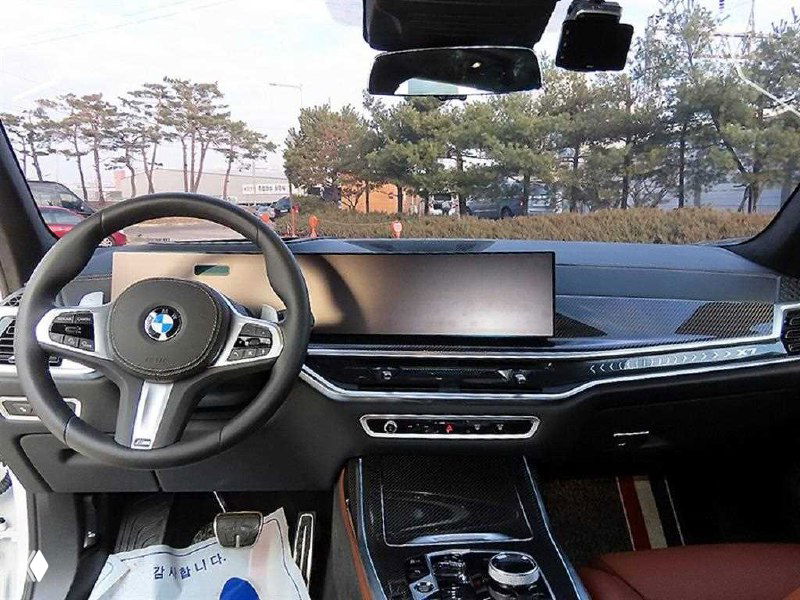 Интерьер BMW X7: вид на руль и широкую цифровую панель, центральная консоль и переднее кресло, салон на стоянке